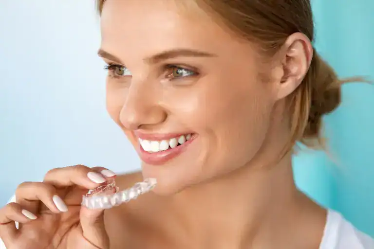 A smiling woman holding a clear dental aligner, promoting orthodontic dental care.